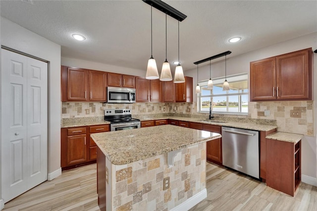 kitchen featuring hanging light fixtures, appliances with stainless steel finishes, brown cabinets, and a sink