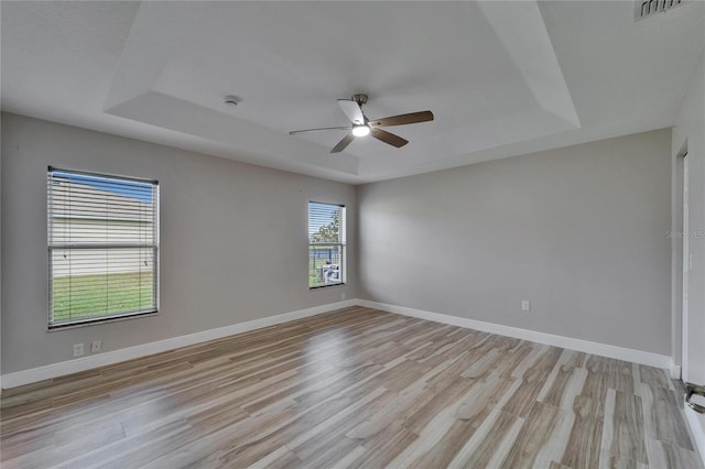 empty room with a tray ceiling, visible vents, light wood finished floors, and baseboards