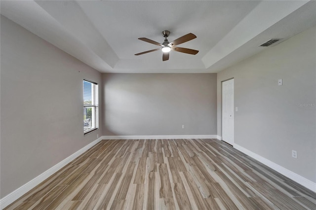 empty room featuring ceiling fan, visible vents, light wood-style floors, baseboards, and a raised ceiling