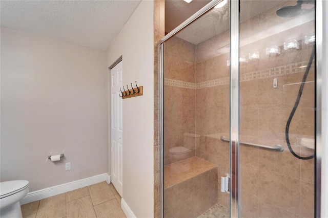 bathroom with baseboards, toilet, a textured ceiling, a shower stall, and a closet