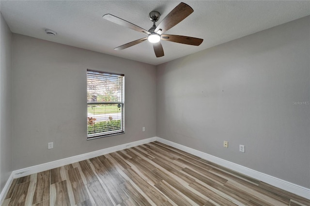 empty room with a textured ceiling, light wood-type flooring, a ceiling fan, and baseboards