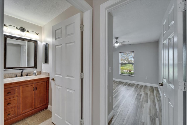 bathroom featuring a textured ceiling, wood finished floors, a ceiling fan, vanity, and baseboards