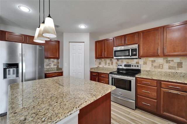 kitchen with stainless steel appliances, hanging light fixtures, and light stone counters