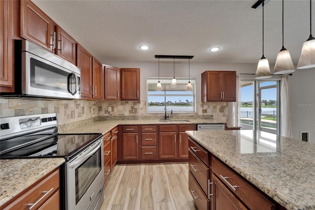 kitchen featuring stainless steel appliances, a sink, light stone countertops, and pendant lighting