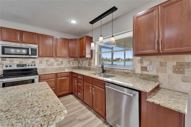 kitchen featuring light stone counters, pendant lighting, decorative backsplash, appliances with stainless steel finishes, and a sink