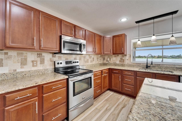 kitchen featuring light stone counters, stainless steel appliances, a sink, brown cabinets, and pendant lighting