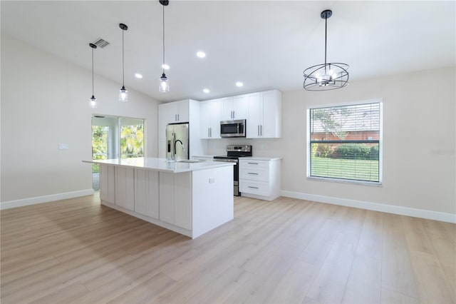 kitchen with appliances with stainless steel finishes, an island with sink, light hardwood / wood-style floors, pendant lighting, and white cabinetry