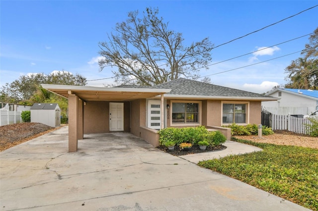 view of front of home featuring an outdoor structure, concrete driveway, stucco siding, a carport, and a shed