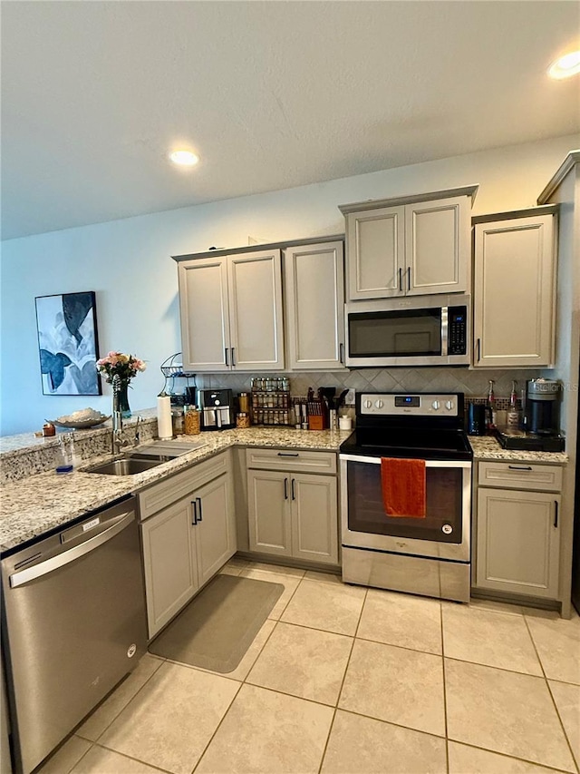 kitchen with appliances with stainless steel finishes, gray cabinets, light tile patterned flooring, and a sink