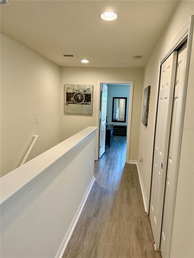 hallway with recessed lighting, baseboards, wood finished floors, and an upstairs landing