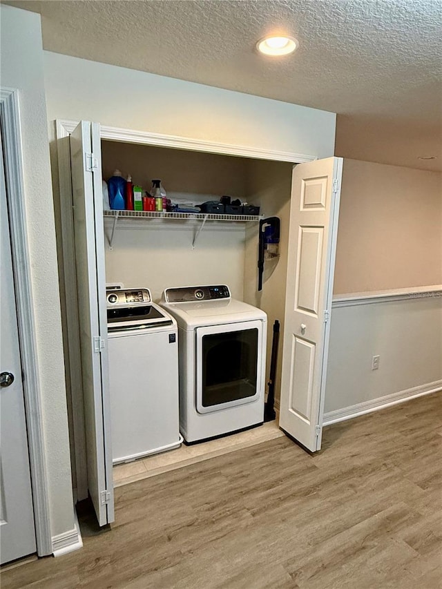 washroom with light wood finished floors, laundry area, washer and clothes dryer, and a textured ceiling