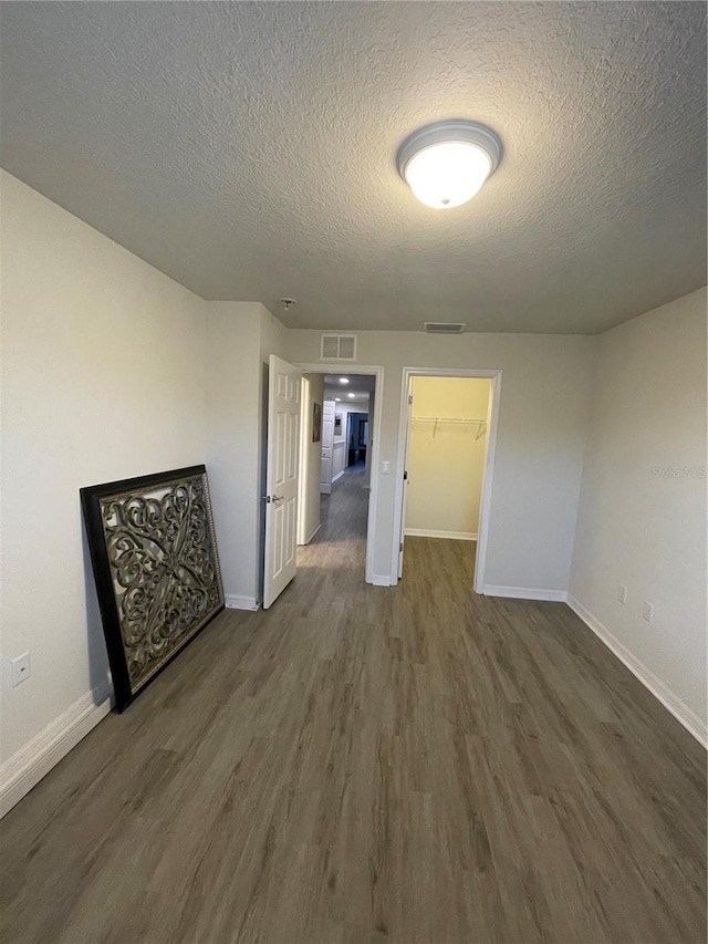 unfurnished bedroom featuring baseboards, a textured ceiling, visible vents, and dark wood-type flooring