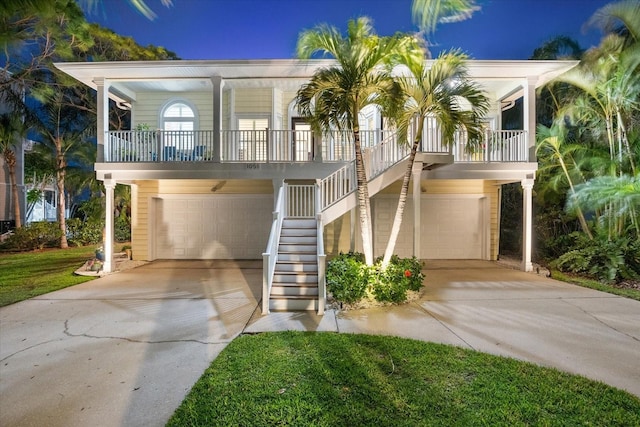 beach home featuring a porch, stairway, concrete driveway, and a garage