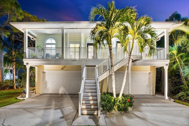 coastal inspired home featuring a porch, an attached garage, concrete driveway, and stairs