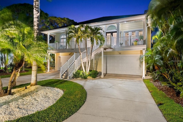 coastal home with stairs, concrete driveway, a garage, and covered porch