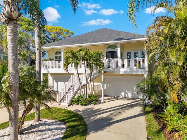 coastal inspired home with stairs, covered porch, french doors, a garage, and driveway