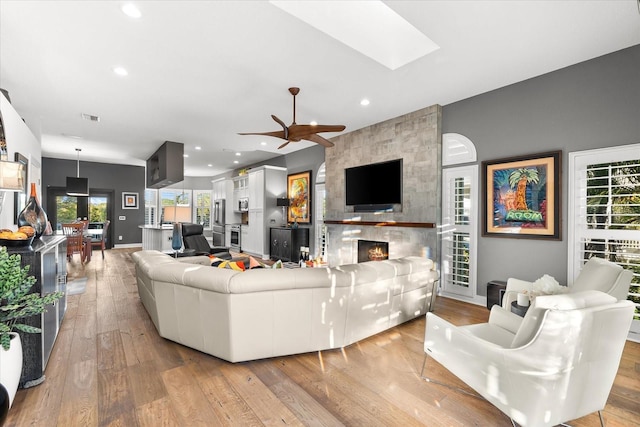 living room featuring visible vents, ceiling fan, hardwood / wood-style floors, a fireplace, and a skylight