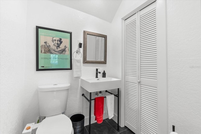 bathroom with tile patterned floors, toilet, a textured wall, and a closet