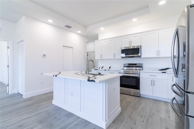 kitchen with an island with sink, appliances with stainless steel finishes, white cabinets, and light hardwood / wood-style floors