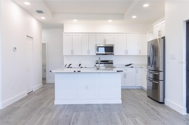 kitchen featuring a center island with sink, white cabinetry, a tray ceiling, light hardwood / wood-style floors, and stainless steel appliances