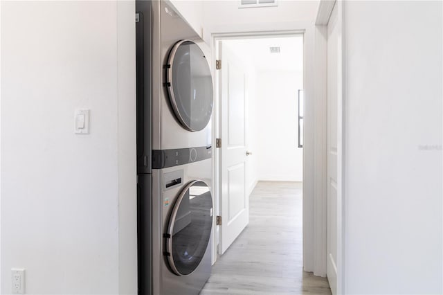 clothes washing area featuring light hardwood / wood-style floors and stacked washer / drying machine