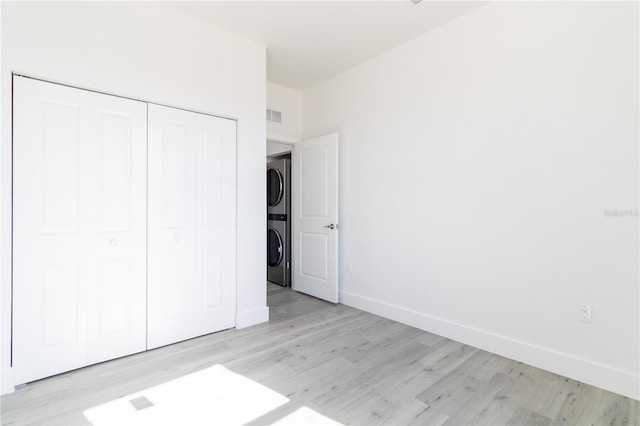 unfurnished bedroom with light wood-type flooring, a closet, and stacked washer and dryer