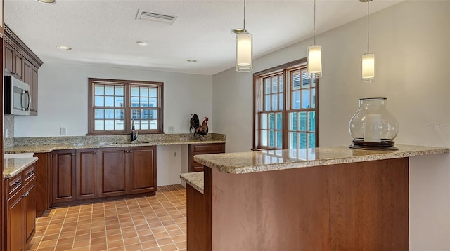 kitchen with decorative light fixtures, stainless steel microwave, visible vents, a sink, and a peninsula