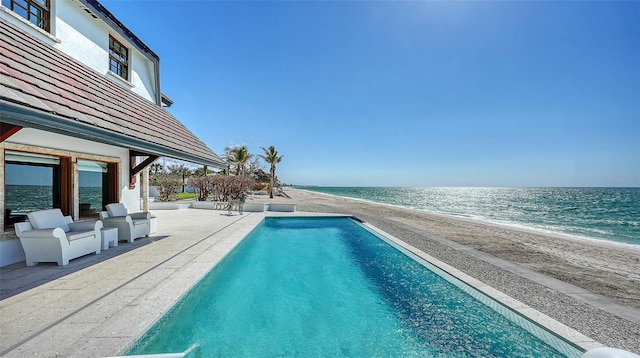 outdoor pool featuring a water view, a patio area, and a beach view