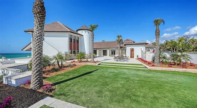 rear view of house featuring a patio area, a lawn, a water view, and stucco siding