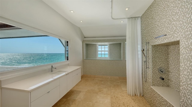 bathroom with a tile shower, a sink, lofted ceiling, and wallpapered walls