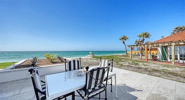 view of patio / terrace featuring a water view, a beach view, outdoor dining area, and a pergola