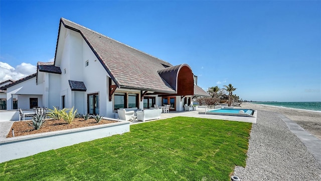 rear view of property with an outdoor pool, a lawn, a water view, a patio area, and a view of the beach