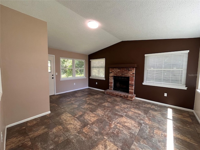 unfurnished living room with a brick fireplace, vaulted ceiling, a textured ceiling, and baseboards