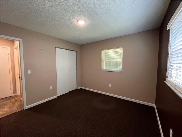 unfurnished bedroom featuring baseboards, dark colored carpet, and a textured ceiling