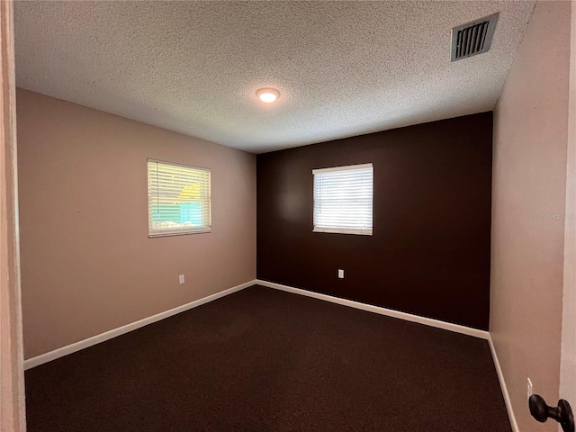 empty room featuring baseboards, visible vents, dark carpet, and a textured ceiling