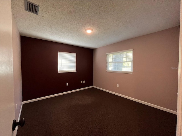 empty room featuring a textured ceiling, dark carpet, visible vents, and baseboards