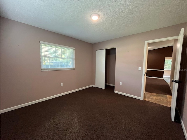 unfurnished bedroom with dark colored carpet, multiple windows, and a closet