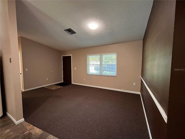 empty room with baseboards, visible vents, vaulted ceiling, a textured ceiling, and dark carpet