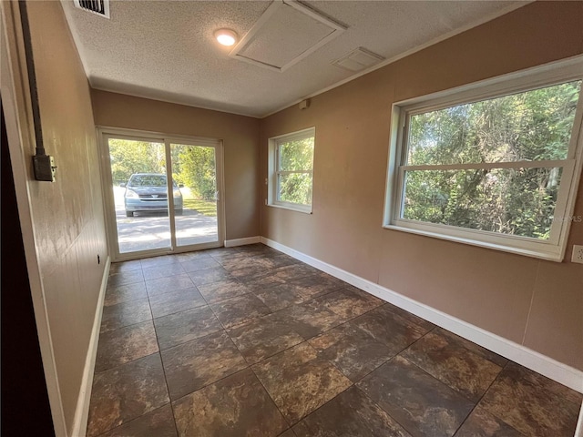 empty room featuring attic access, visible vents, a textured ceiling, and baseboards