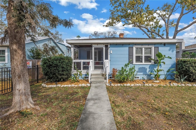 bungalow-style house featuring a chimney, a sunroom, crawl space, fence, and a front lawn