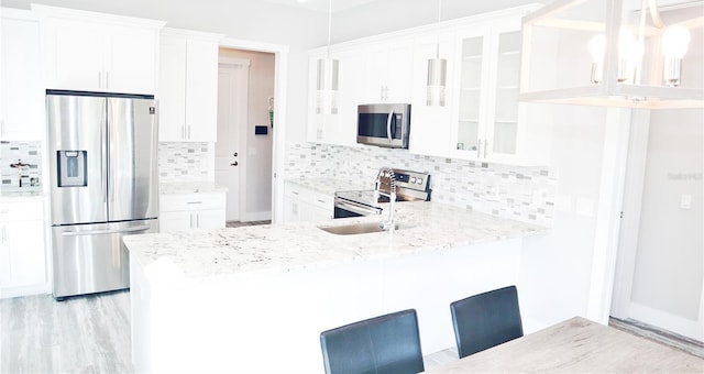 kitchen with stainless steel appliances, a peninsula, white cabinets, hanging light fixtures, and glass insert cabinets