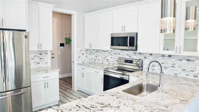 kitchen featuring stainless steel appliances, a sink, white cabinetry, tasteful backsplash, and glass insert cabinets