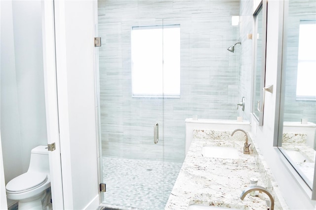 full bath with toilet, a shower stall, double vanity, and a sink