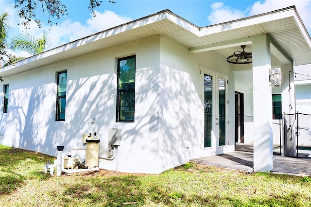 view of side of home featuring a ceiling fan, french doors, a lawn, and stucco siding