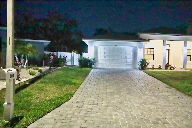 view of front of house with decorative driveway, stucco siding, an attached garage, a front yard, and fence