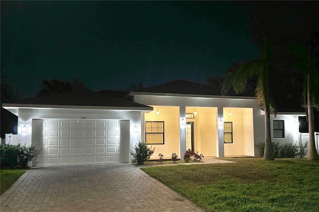 view of front of home with a garage, stucco siding, decorative driveway, and a yard