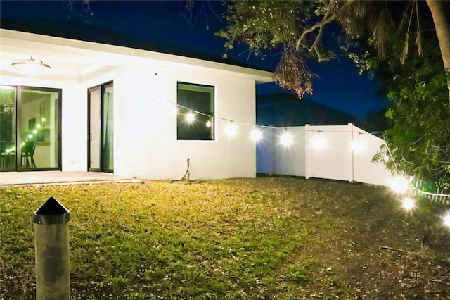 property exterior at twilight with a lawn, fence, and stucco siding