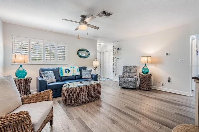 living room featuring baseboards, a ceiling fan, visible vents, and light wood-style floors