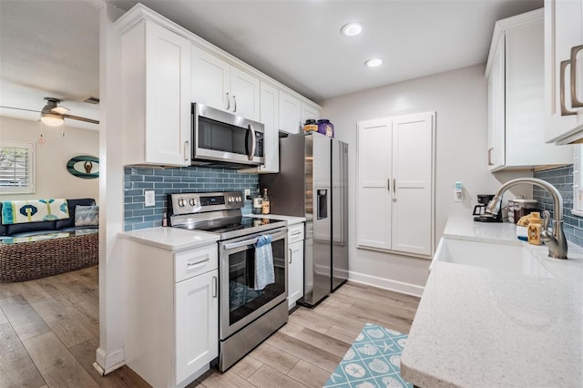 kitchen featuring light wood finished floors, tasteful backsplash, white cabinets, appliances with stainless steel finishes, and a sink