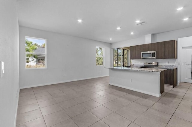 kitchen with a center island with sink, light tile patterned floors, recessed lighting, appliances with stainless steel finishes, and baseboards